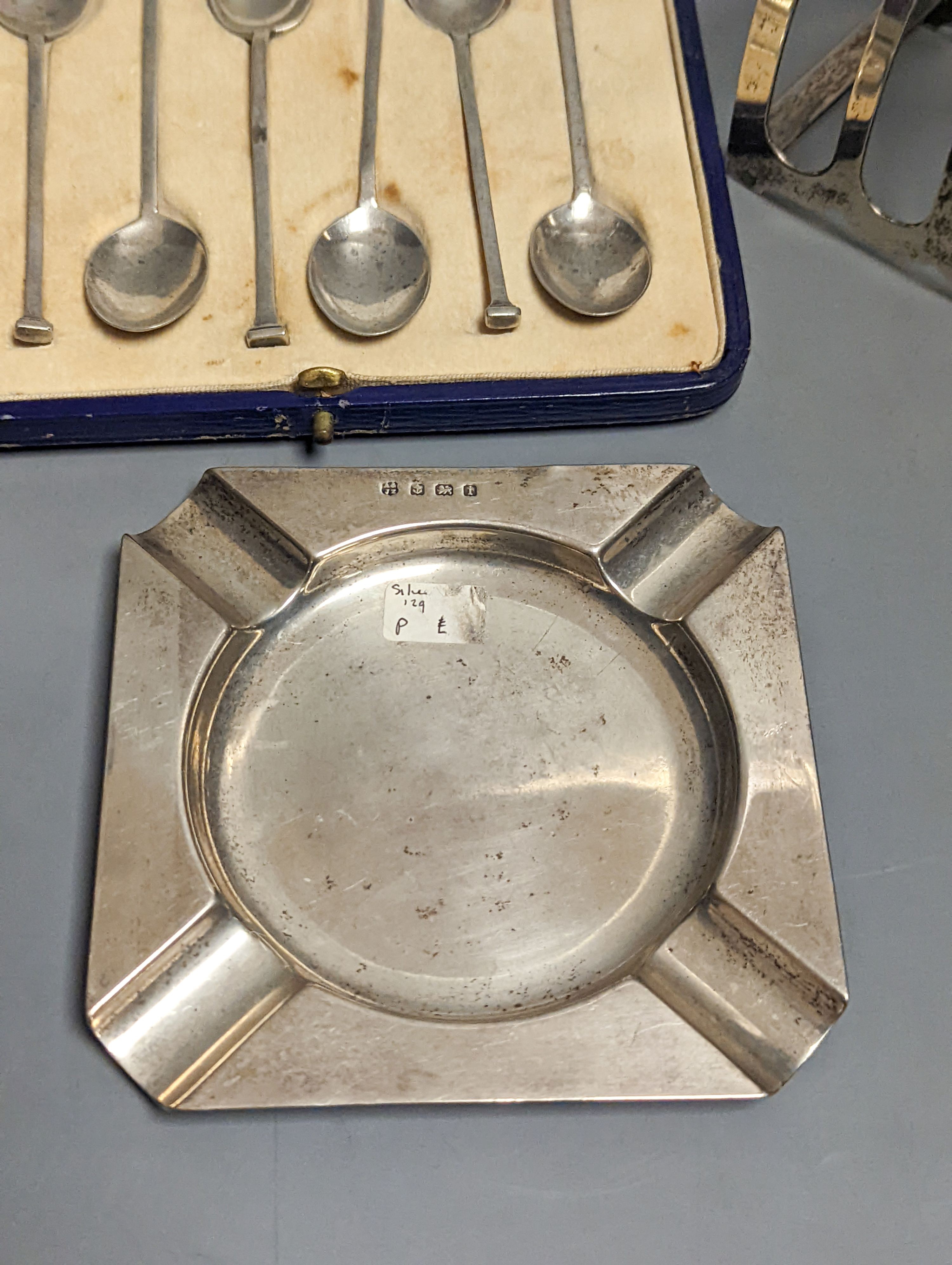 A pair of Edwardian glass handled silver salad servers, William Hutton & Sons, London, 1902, 26.8cm, a cased set of six silver teaspoons, a silver toastrack and a silver ashtray.
